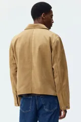 Campera de gamuza sintética color tostado, con cuello camisero, cierre frontal, bolsillo superior con cierre y bolsillos laterales ribeteados.