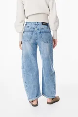 Jean de corte wide leg y tiro medio, con diseño de costuras laterales curvadas que le otorgan una silueta redondeada. Presenta un lavado azul claro con efecto desgastado, cierre frontal con botón y bolsillos laterales.