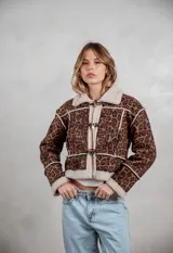 Campera de gamuza con estampado animal print de leopardo, forrada en corderito sintético color crema. Presenta cierre frontal con botones tipo toggle, cuello solapa y detalles de costuras visibles.