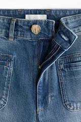 Jean de tiro alto en denim de algodón con leve stretch. Presenta piernas amplias, corte holgado, bolsillos tipo parche en la parte frontal y raya marcada a lo largo de las piernas. Incluye cierre y botón metálico.