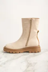 Bota de caña media color crema, confeccionada en cuero. Presenta puntera redondeada, cierre lateral y tirador trasero. Suela track color caramelo.