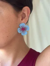 Aro con forma de flor pintada a mano en color celeste, con detalles de trazos brillantes en tonos rojizos y centro decorado con mostacillas.