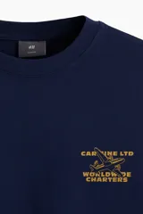 Remera azul marino de corte holgado con cuello redondo y estampado pequeño en el pecho con un avión y texto en color ocre.