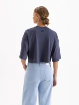 Remera blanca de corte cropped y manga corta, confeccionada en algodón. Presenta una estampa frontal con un conejo con estampado animal print sobre una nube y el texto 'IL BUNNY' en color amarillo.