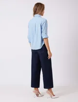 Camisa de algodón y lyocell, marca Weekend Routine, color celeste con finas rayas blancas. Tiene cuello con solapa, botones metálicos en la abertura frontal y mangas largas regulables con presilla y botón. La espalda presenta un canesú horizontal con un tablón central, y el bajo es asimétrico y redondeado.