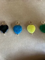 Dije con forma de corazón de piedra sintética en varios colores con gancho metálico dorado.