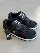 Championes DC modelo Manteca 4, color negro con detalles en rojo y blanco. Presentan una combinación de materiales que incluyen malla transpirable y cuero sintético, con el logo de DC en la lengüeta y una suela blanca.