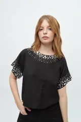 Blusa de manga corta color negro con escote redondo, decorada con pedrería brillante en el cuello y en los bordes de las mangas.