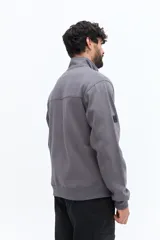 Buzo de algodón color terracota, con cuello alto y cierre parcial frontal. Presenta puños y cintura ajustados, bolsillos laterales y un pequeño logo bordado en el pecho.