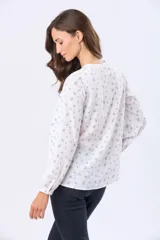 Blusa de manga larga con cuello redondo y cierre frontal de botones. Presenta un estampado floral en color negro sobre fondo blanco.