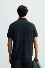 Polo de manga corta color blanco roto, con cuello solapa y cierre frontal de cremallera. Presenta un tejido de piqué estructurado y corte regular fit.