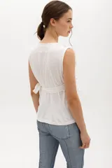 Musculosa cruzada de color beige, con escote en V y volados decorativos en los hombros y el frente.