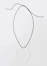 Collar de diseño minimalista compuesto por un cordón de cuero negro ajustable mediante lazo y un dije circular grande de metal plateado.