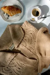 Sweater de punto color gris claro, con cuello amplio tipo solapa y detalles de tejido crochet en los hombros y mangas. Presenta mangas largas con puños ajustados y diseño de corte holgado.