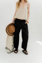 Pantalón negro de lino y algodón, de tiro medio o bajo, con pinzas frontales y pretina ancha en la espalda con cambio de color y vivo en contratono. Presenta cortes en la mitad de la pierna en la espalda, cierre frontal con cremallera y botón, y bolsillos delanteros.