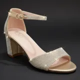 Sandalia de tacón cuadrado medio, color dorado, con tiras cubiertas de pedrería brillante. Presenta cierre de pulsera con hebilla metálica en el tobillo y puntera abierta.