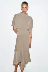 Top fluido color beige, con cuello perkins y mangas por debajo del codo. Bajo redondeado.