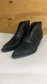 Botines negros de cuero con punta fina, caña baja y cierre lateral con cremallera. Presentan apliques de tachas metálicas plateadas. El taco es de altura media.