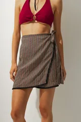 Falda corta tipo pareo con diseño envolvente, confeccionada en tela con estampado de rayas verticales en tonos tierra. Cuenta con un lazo lateral para ajuste y un borde inferior con detalle de costura en contraste.