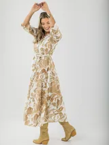 Vestido camisero midi de algodón con estampado floral en tonos rosados y blancos. Tiene cuello camisero, mangas 3/4, botones frontales, falda escalonada y cinturón fino.