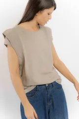 Remera sin mangas de corte holgado, con hombreras marcadas que crean un efecto de manga corta estructurada. Presenta un diseño minimalista con frunces laterales en la cintura y cuello redondo.