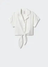 Camisa blanca de lino con cuello camisero, manga corta con vuelta, diseño crop y oversize. Tiene un bolsillo de parche en la parte delantera, cierre de botones y lazo ajustable.