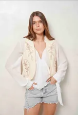 Chaleco blanco de corte corto, con bordados florales en tono tostado en la parte delantera.