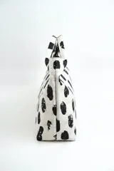 Cartera estilo hobo de color crudo con estampado de manchas negras abstractas, cierre superior y correa de hombro ajustable de cuero negro.