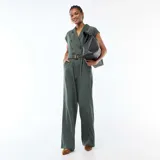 Mono pantalón verde oscuro con solapas, cierre cruzado de doble botonadura, mangas cortas con hombreras sutiles, bolsillos laterales y pantalón de corte recto y holgado. Incluye cinturón a juego con hebilla carey.