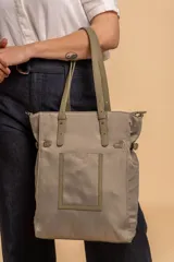 Bolso tipo tote bag de símil cuero color rosa pálido, con asas dobles y detalles de costura en color beige claro. Presenta un bolsillo frontal rectangular aplicado y herrajes metálicos.