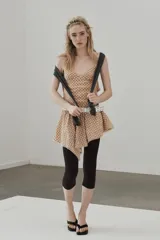 Vestido corto con escote en V y tirantes finos ajustables, confeccionado en tejido a cuadros beige y rojo. La falda es asimétrica y presenta un bajo con detalle de encaje.