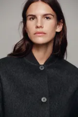 Cazadora bomber beige confeccionada en hilatura con lana, con cuello subido, manga larga y bolsillos frontales. Presenta cierre frontal con botones oscuros y puños, cuello y ruedo en tejido rib.