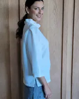 Camisa de manga tres cuartos color beige con cuello con volados y botones frontales. Presenta un detalle de color negro en la parte superior de las mangas.