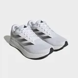 Championes de running Adidas Duramo RC, color blanco con las tres franjas laterales en gris metalizado. Presentan una capellada de malla transpirable y una suela gruesa de EVA blanca con detalles en negro en la parte inferior.