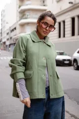 Chaqueta de lana afieltrada en color amarillo mostaza, con cuello camisero, cierre frontal con broches a presión y bolsillos delanteros. Presenta un diseño de espalda con apertura para mayor movimiento.