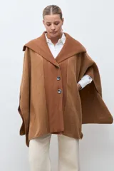 Capa de paño color marrón con cuello solapa y panel central de tejido acanalado. Cuenta con cierre frontal de tres botones grandes y diseño holgado.