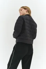 Campera acolchada negra, de nylon guateado, con cuello redondo y cierre frontal de botones a presión. Presenta bolsillos laterales discretos y elástico fino en los puños.
