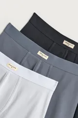 Pack de tres calzoncillos tipo bóxer de tejido elástico con acabado aterciopelado, en colores gris claro, gris oscuro y negro, con cintura elástica y etiqueta decorativa frontal.