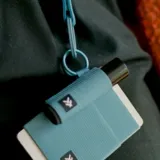 Llavero porta labial celeste con logo blanco estampado y aro metálico.