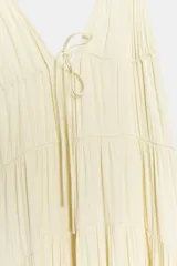 Vestido largo color crudo de tela satinada, con escote en V, tirantes finos ajustables, detalle de cordón ajustable en el pecho y diseño fruncido en capas.