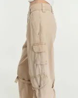 Pantalón cargo de tiro medio confeccionado en gabardina de algodón y lino con efecto gastado. Presenta una silueta de pierna recta y ancha, con bolsillos laterales inclinados y bolsillos cargo con tapa en las rodillas. Incluye tiras ajustables con hebillas metálicas en los laterales para modificar la silueta, cierre metálico y bolsillos traseros.