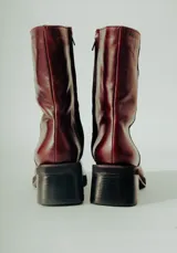 Bota de caña media confeccionada en cuero natural color bordó, con diseño minimalista, punta cuadrada y taco ancho de altura media.