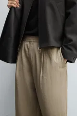 Pantalón negro de corte relajado con cintura elástica ajustable y pliegues en la parte delantera. Presenta bolsillos laterales y bolsillos traseros de parche.