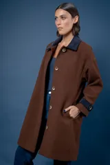 Tapado de paño color marrón, con cuello camisero y puños en contraste de color azul marino. Presenta cierre frontal con botones grandes y bolsillos laterales.