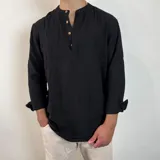Camisa negra de manga larga con cuello mao y tapeta corta con botones de madera. El tejido presenta una textura arrugada o plisada. Las mangas están remangadas y sujetas con una presilla abotonada.