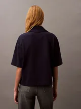 Chomba azul marino de punto de algodón con cuello clásico, tapeta con botones ocultos y mangas cortas. Presenta un corte holgado y un escudo bordado con el logo de Calvin Klein en el pecho.