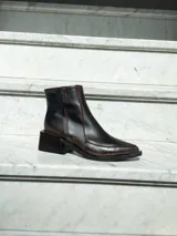 Bota corta de cuero vacuno con acabado envejecido, diseño de punta fina y taco cuadrado de madera. Cuenta con cierre lateral interno.
