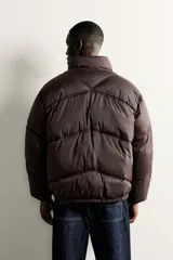 Cazadora acolchada tipo puffer de corte relajado, color negro, con cuello subido, cierre frontal de cremallera y bolsillos laterales con cierre. Presenta puños y ruedo con terminación elástica.