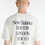 Remera de algodón New Balance International Stamp, color blanco off-white, de corte holgado, manga corta y cuello redondo. Presenta un pequeño estampado gráfico en el pecho con diseño de sellos internacionales y logo de la marca.