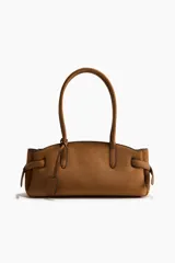 Cartera de hombro color tostado, con doble asa superior y detalle de tiras laterales ajustables. Cuenta con cierre magnético y etiqueta colgante.